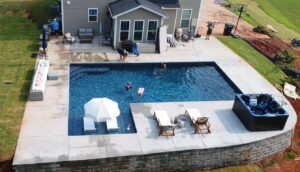 a custom inground vinyl pool in a homeowner's backyard. Deck chairs and a hot tub sit by the edge of the pool.