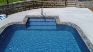 An inground pools with steps and a handrail leading into the water