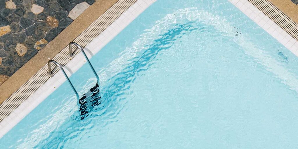 Clear blue water ripples in a fiberglass swimming pool with a stainless steel ladder, showcasing low-maintenance alternative benefits.