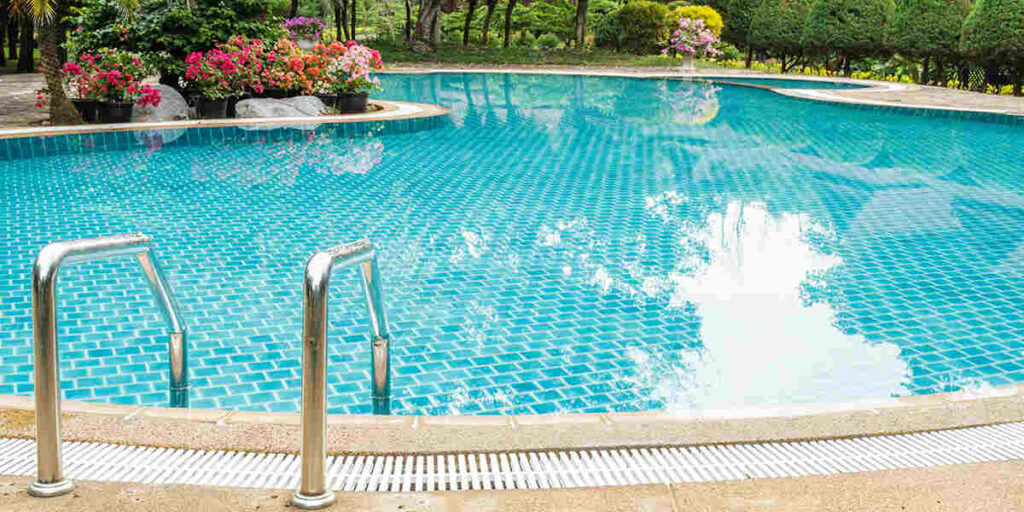 A curved inground swimming pool with turquoise water, stainless steel handrails, and landscaped gardens creates an inviting backyard retreat.