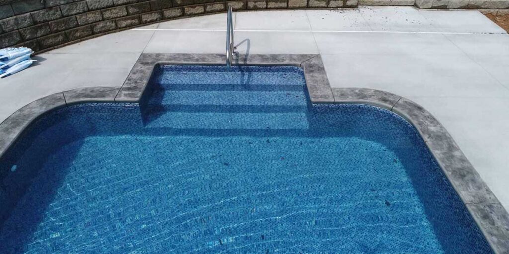 Custom vinyl-over-steel entry steps built into an inground swimming pool featuring a central handrail and blue mosaic pattern liner.